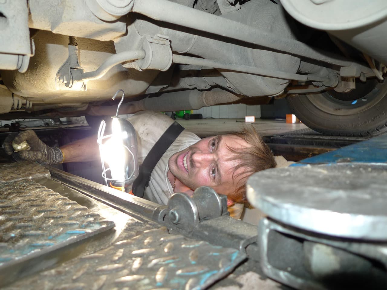 A mechanic under a car with an inspection lamp, looking for the fault
