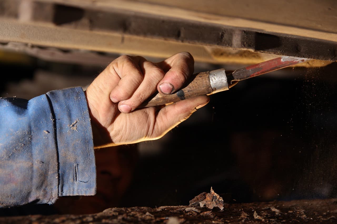 A gloved hand working a tool along the underside of a car